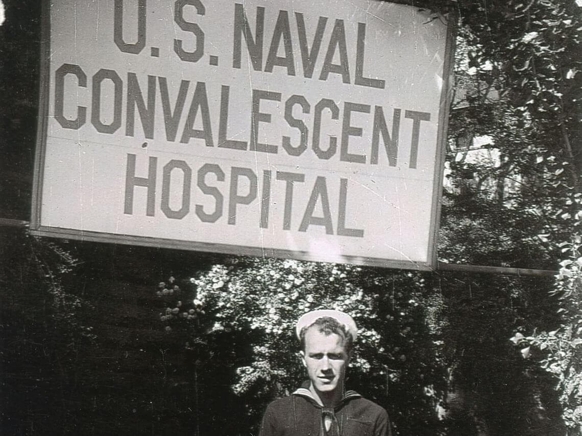 A man in a naval uniform stands in front of a U.S. Naval Convalescent Hospital sign in the 1930's at Hotel Colorado