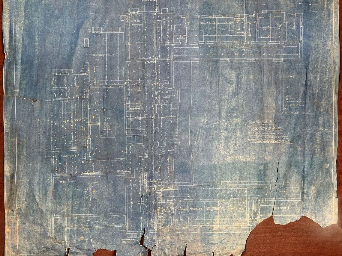 A tattered, vintage blueprint with faded blue and white lines displays architectural plans, reminiscent of designs pivotal in naval history. The paper is worn, with visible tears and creases, lending it an aged and historical appearance.