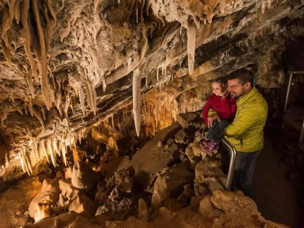 A father holding his child standing inside a Glenwood Caverns Adventure Park cave adorned with stalactites and stalagmites