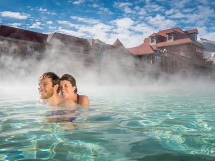 A couple enjoys swimming in a steaming outdoor pool under blue sky at Glenwood Hot Springs