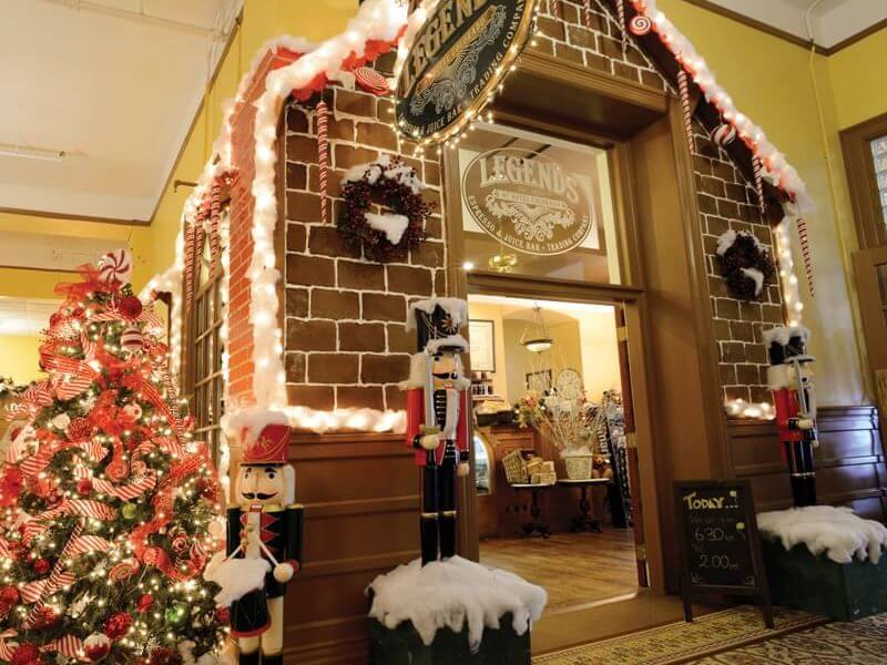 A reimagined festive storefront dazzles with candy cane accents and two nutcracker statues flanking the entrance. A Christmas tree adorned with lights and ornaments stands to the left, enhancing the cozy, cheerful atmosphere.