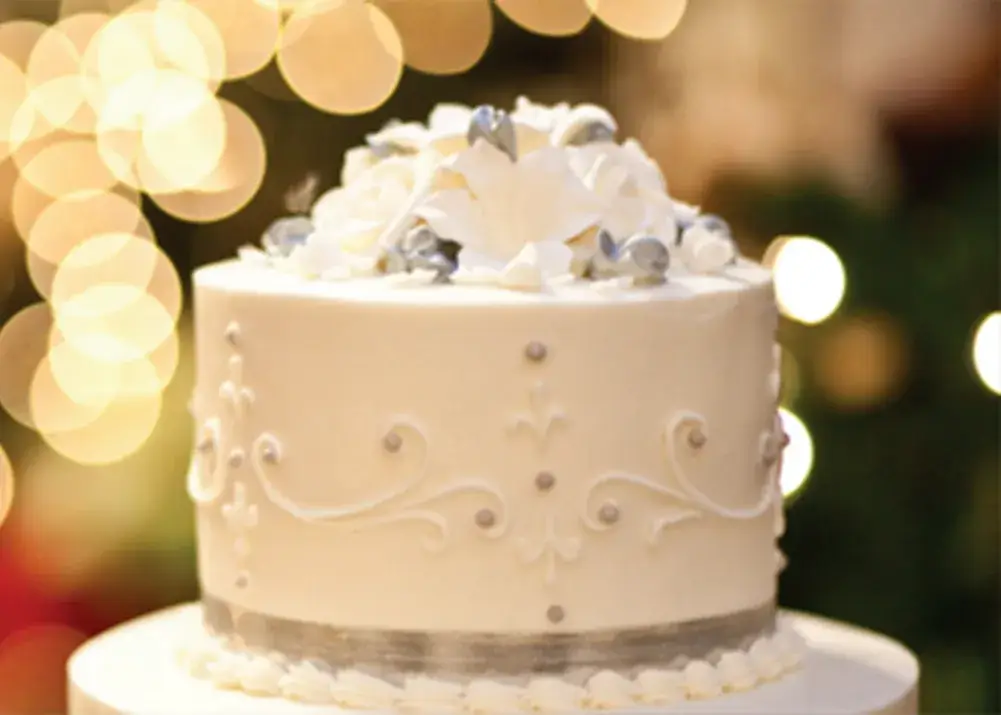 A white frosted cake adorned with intricate icing patterns and large white flowers at Hotel Colorado wedding