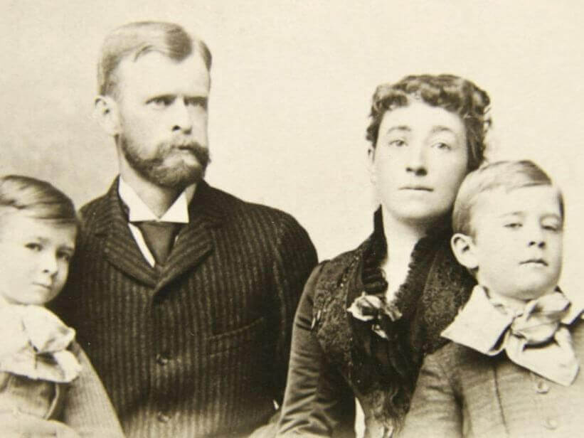 A vintage photograph of the Walter family, featuring a couple with two young boys. The father sports a mustache and beard, while the mother wears a high-collared dress. Both boys have short hair and wear bow ties with jackets against a plain backdrop.