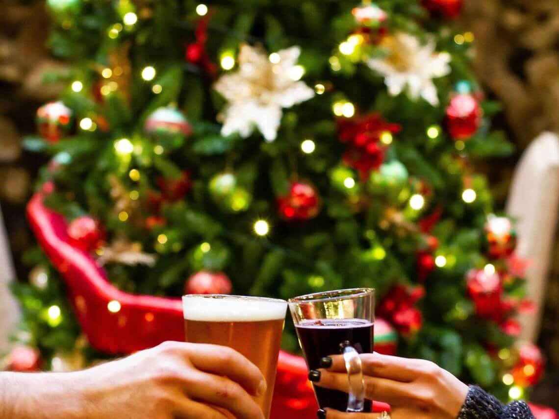 Two people toast in front of a beautifully decorated Christmas tree