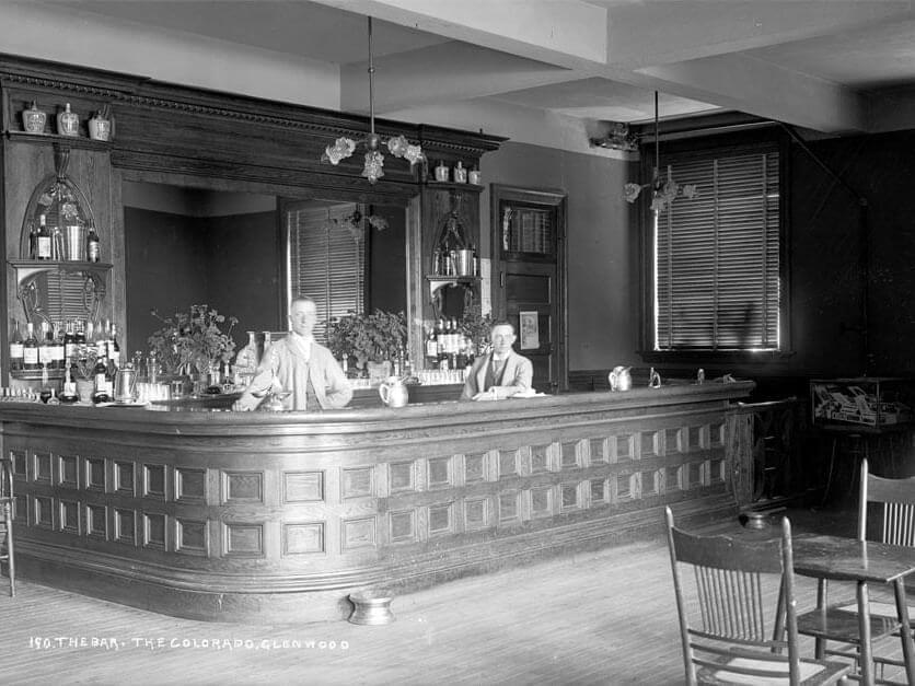 A black-and-white photo of two men standing behind a wooden bar at Hotel Colorado