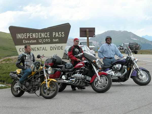 Three motorcyclists parked in front of Independence Pass sign, Elevation 12,095 feet, Continental Divide