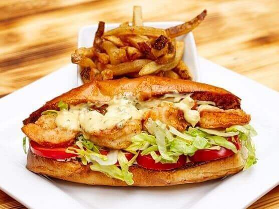 A chef's creation: a sandwich filled with shrimp, lettuce, tomatoes, and sauce, served on a rectangular plate alongside golden-brown fries on a wooden table.