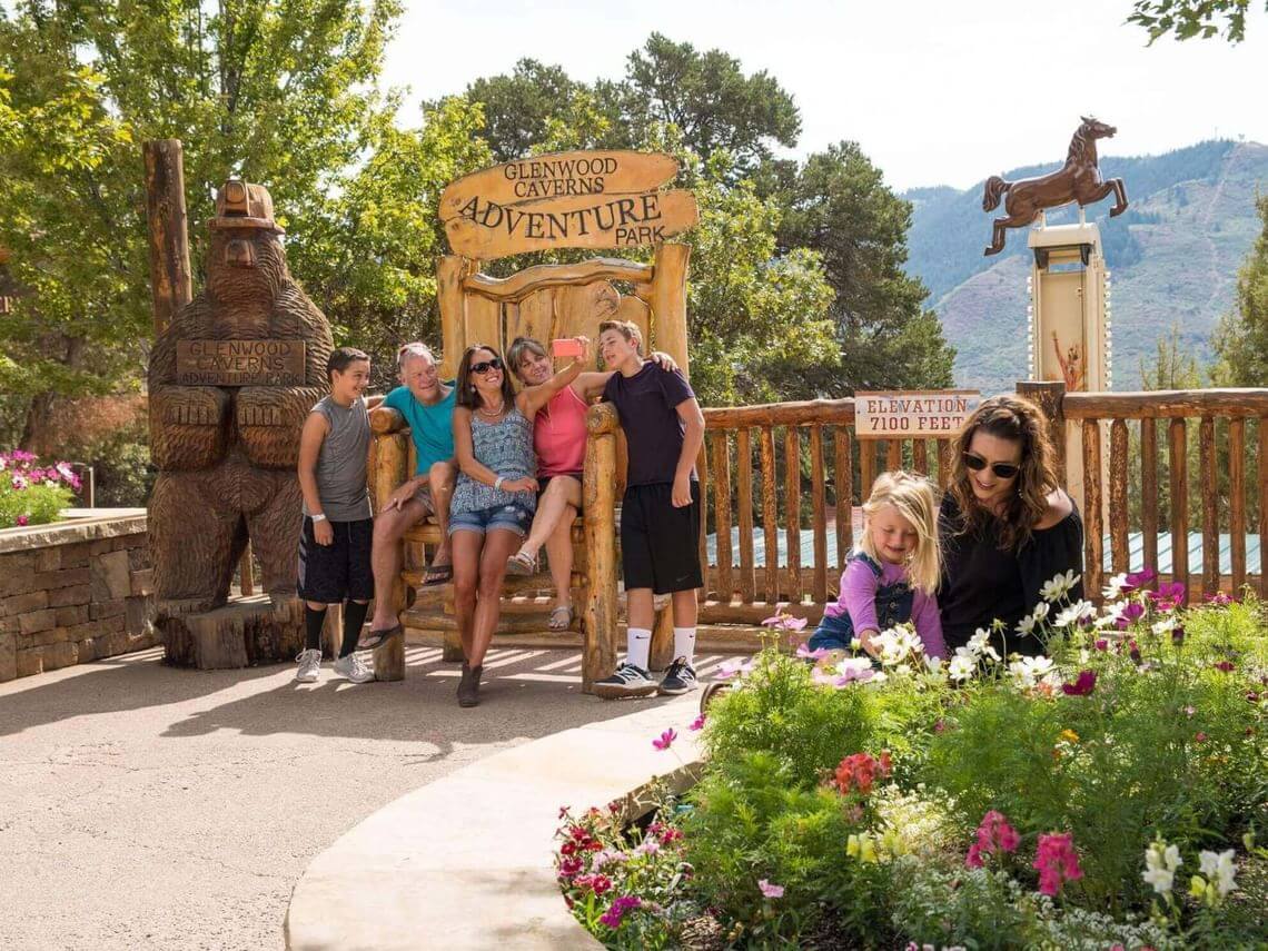 A group of people gather around a wooden chair at Glenwood Caverns Adventure Park