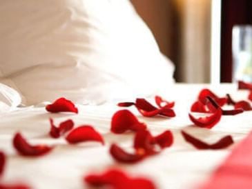 Bed adorned with scattered red rose petals on crisp white sheets at Hotel Colorado