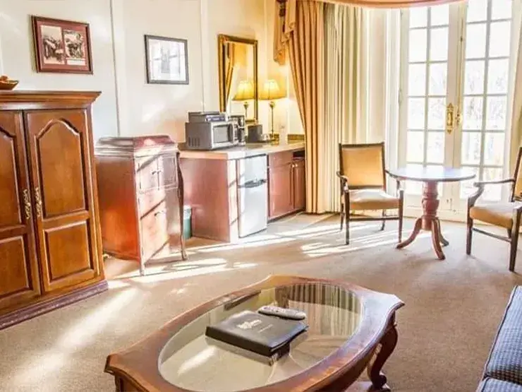 A Classic Suite at Hotel Colorado features a wooden armoire, a round table with two chairs, and a coffee table