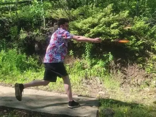 Aman in a floral shirt and shorts throwing a frisbee at Colorado Mountain College disc golf course