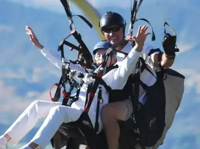 An elderly woman and an instructor are tandem paragliding with wide smiles near Glenwood Springs, Colorado