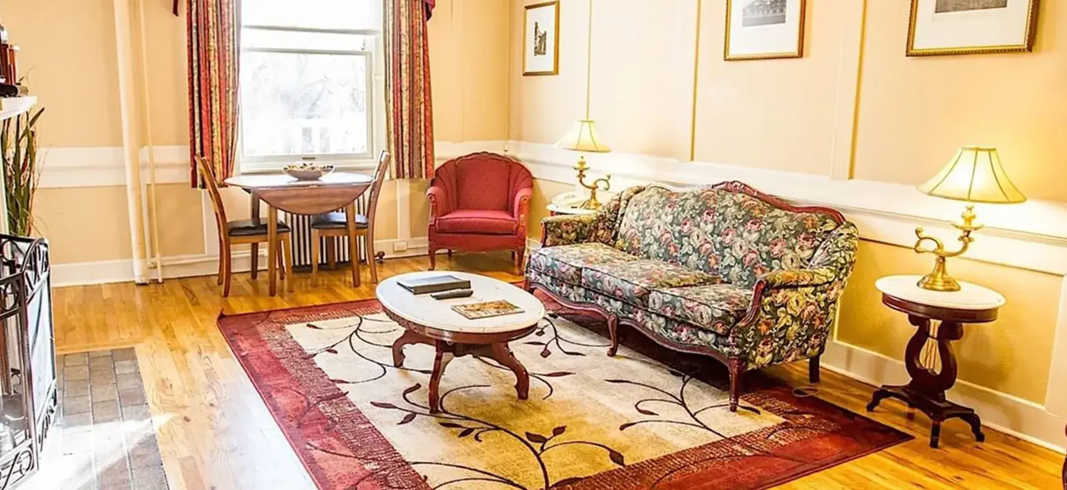 A cozy living room showcases a floral-patterned sofa and red armchair around a wooden coffee table in a Signature Suite at Hotel Colorado