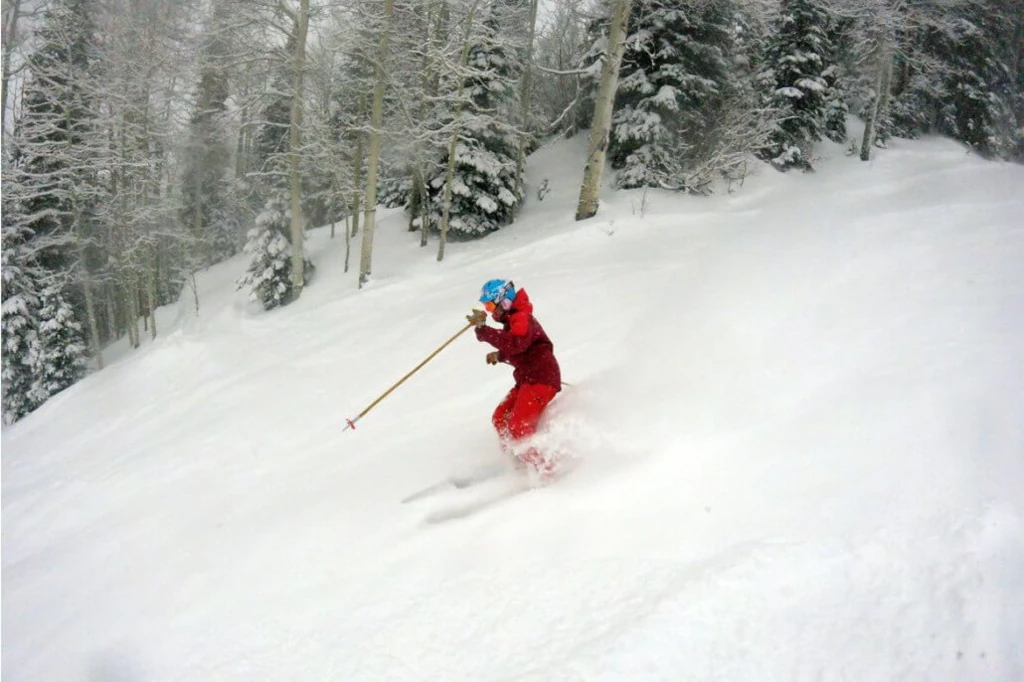 A skier in a red outfit and blue helmet gracefully slices through snow at Sunlight Mountain