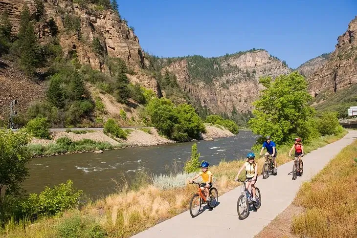 A family of four enjoys a summer bike ride on a paved path along the Colorado River in Glenwood Canyon