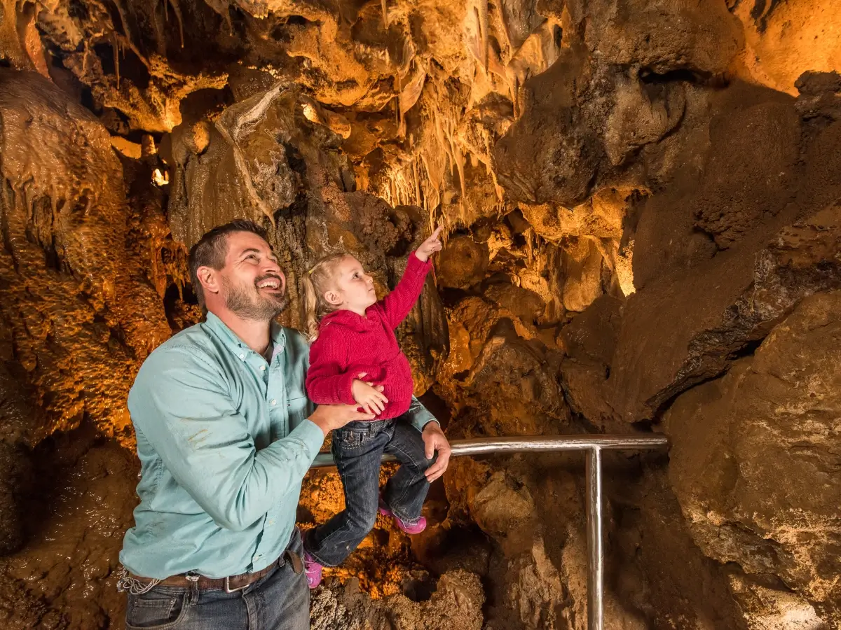 A man holds a young child who is pointing at stalactites inside a Glenwood Caverns cave