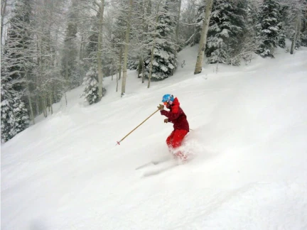 A skier in a red outfit and blue helmet gracefully slices through snow at Sunlight Mountain