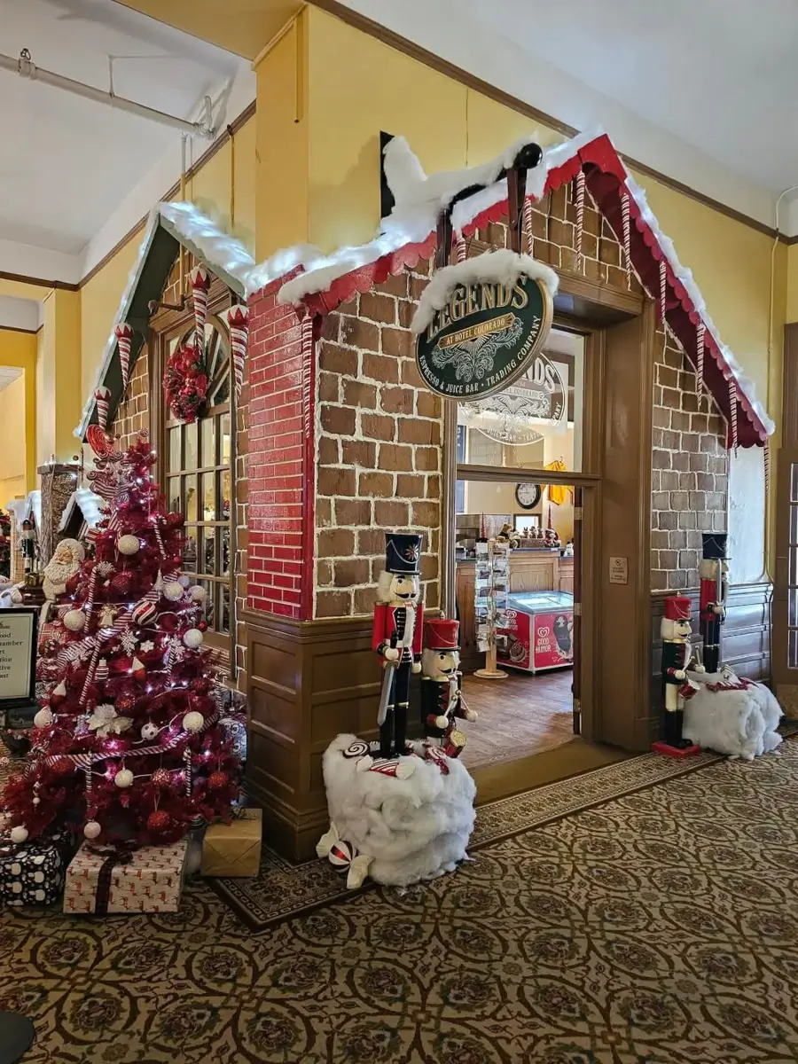 Festive indoor Christmas display featuring a charming gingerbread house facade with a red and white theme. Nutcracker figures stand proudly beside a decorated Christmas tree adorned with pink ornaments, while a sign reading Legends 1894 adds to the cozy holiday atmosphere.