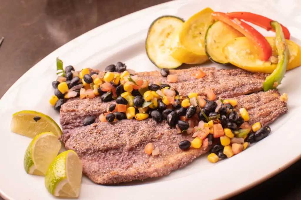 A plate with grilled trout topped with corn, black beans, and diced tomatoes
