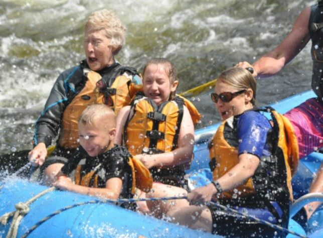Four people wearing life jackets ride a blue raft through whitewater rapids near Glenwood Springs, looking excited and joyful as water splashes over them on a sunny getaway.