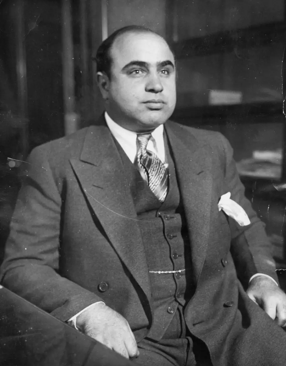 Al Capone in a suit and tie sitting in a chair.
