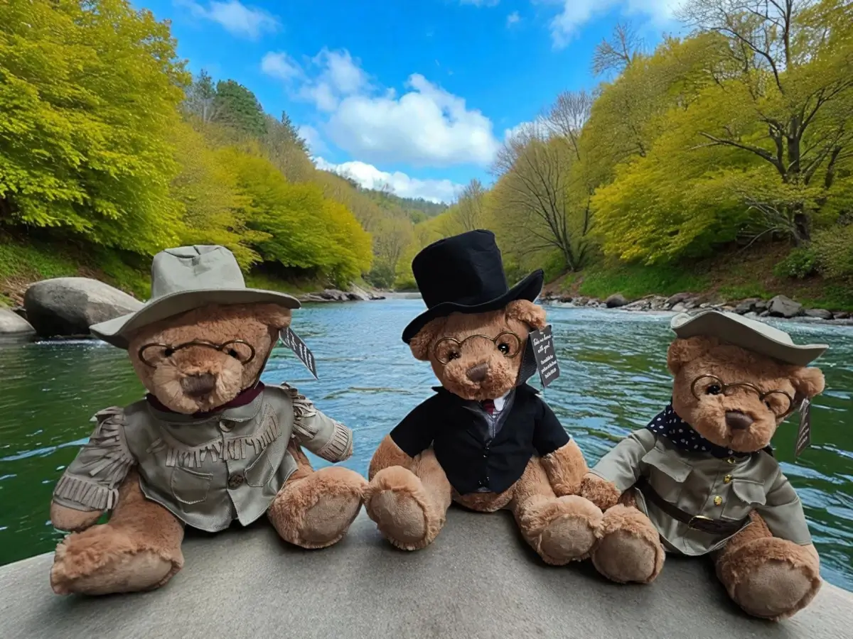 Three teddy bears dressed in old-fashioned outfits sit side by side on a rock, with a river and lush green trees.