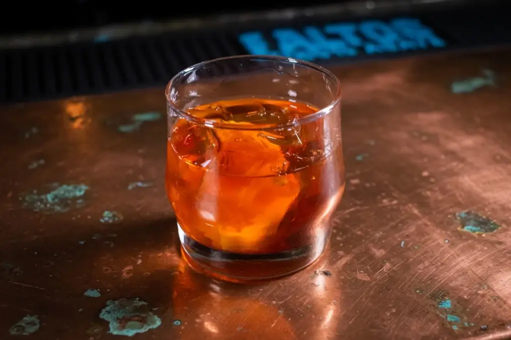 A glass of amber-colored cocktail with ice sits on the Coppertop Bar at Hotel Colorado.