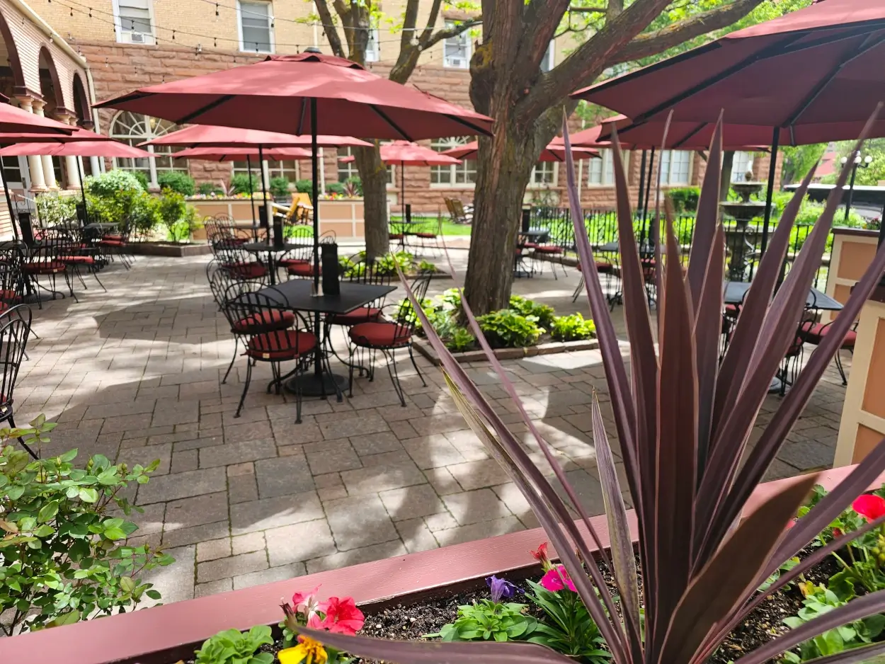 Outdoor patio at Hotel Colorado with black metal tables and chairs, each shaded by large red umbrellas.